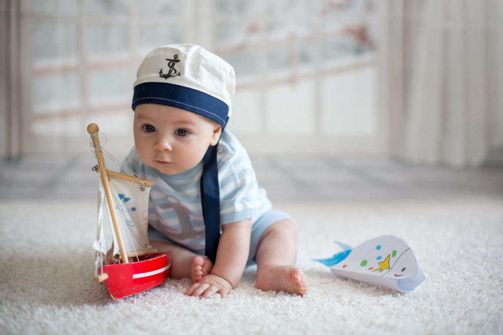 Little baby boy wearing sailor hat, playing with little boat and little fish at home