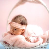 baby girl wearing a pink ribbon and laying on her tummy on a fuzzy blanket in a white basket