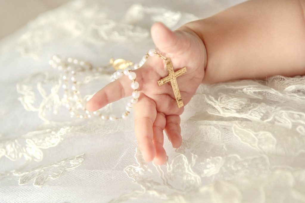 close up of chubby baby fingers holding a pearl Catholic rosary with gold cross