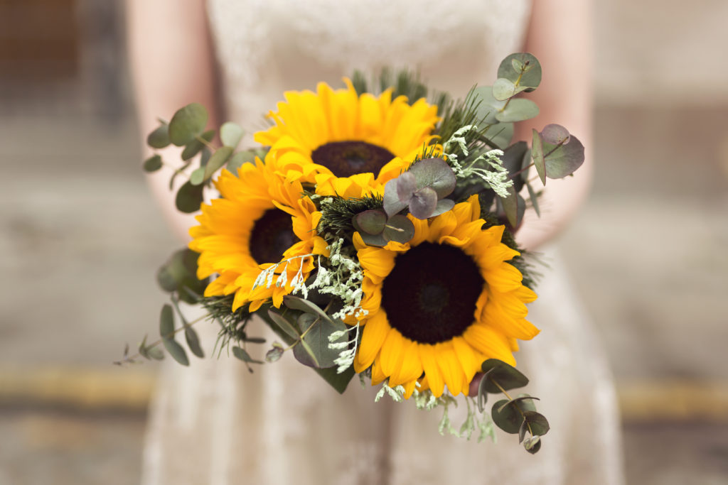 Close up of a bride in a wedding dress holding a sunflower wedding bouquet. Selective focus