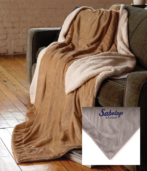 Custom embroidered oversized sherpa blanket draped over gray couch